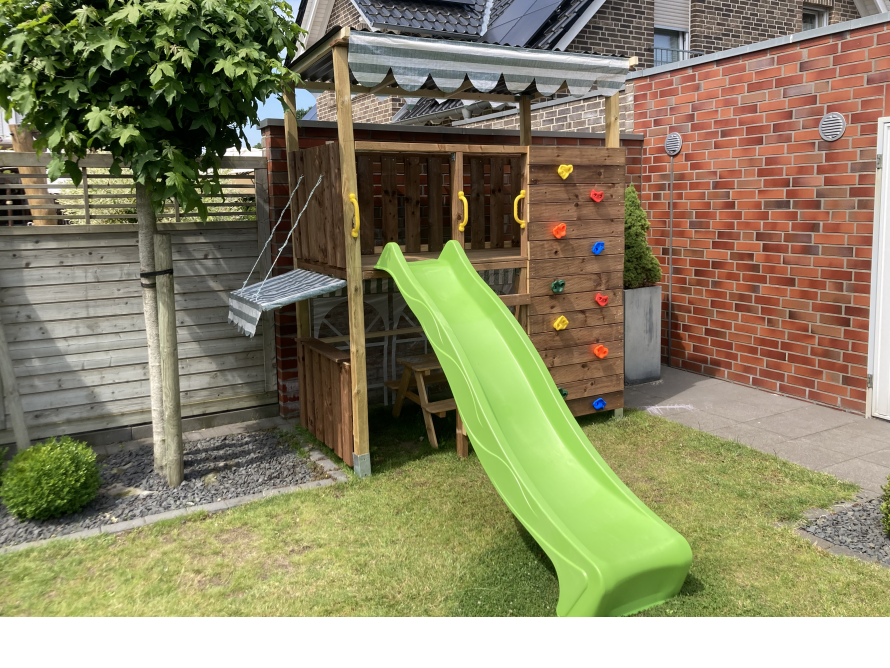 Ein Holzturm mit Rutsche und Kletterwand im Garten.