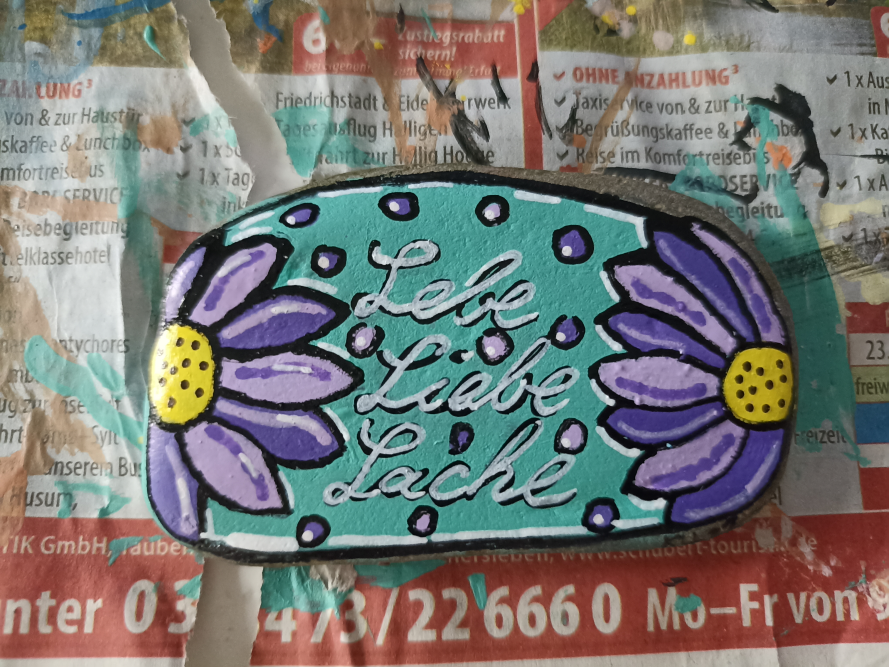Bemalter Stein mit Blumen und dem Schriftzug Lebe Liebe Lache