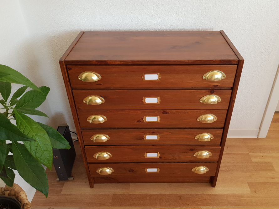 Eine Kommode aus dunklem Holz mit sechs Schubladen und goldenen Griffen.