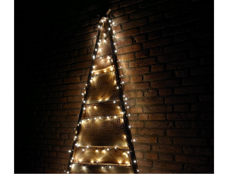 Rustikaler Holz-Weihnachtsbaum mit Lichterkette an Backsteinwand