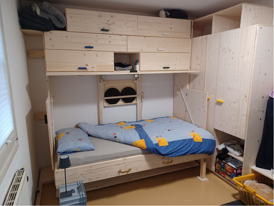 Ein hochklappbares Bett aus hellem Holz mit Schränken.