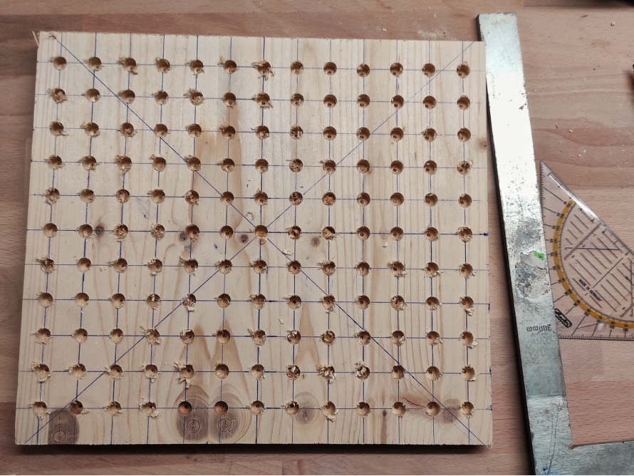 Lochplatte aus Holz mit Bleistiftmarkierungen und einem Anschlagwinkel