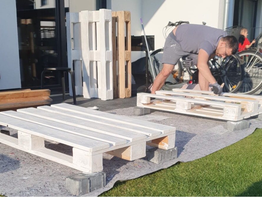 Person streicht Holzpaletten weiß