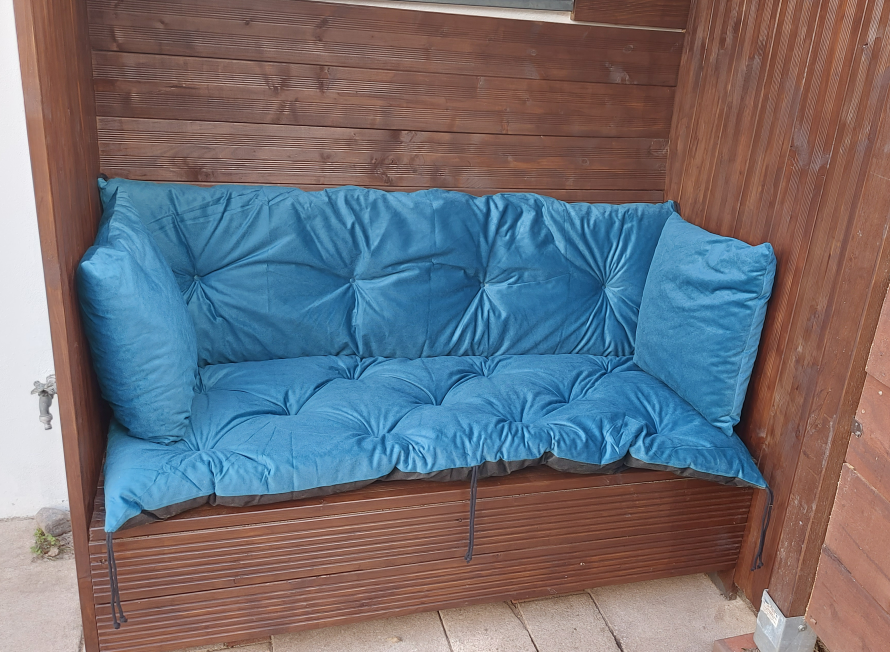 Holzbank mit blauer Sitzauflage in Gartenhütte