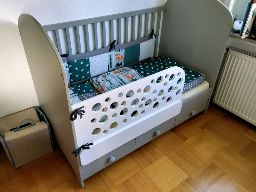 Graues Kinderbett mit Rautenmuster und Nestchen