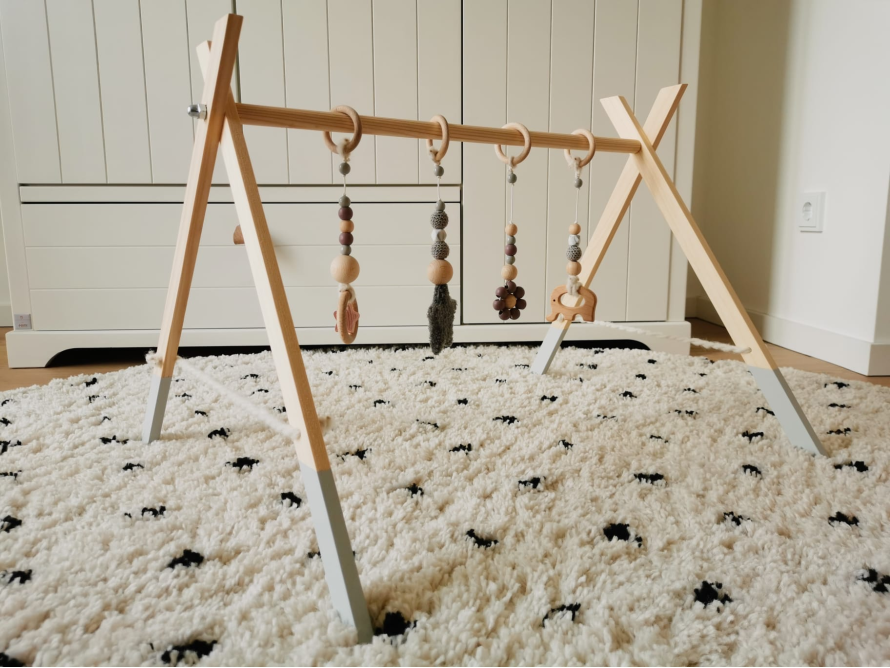 Ein Baby-Spielbogen aus Holz mit daran befestigtem Spielzeug.