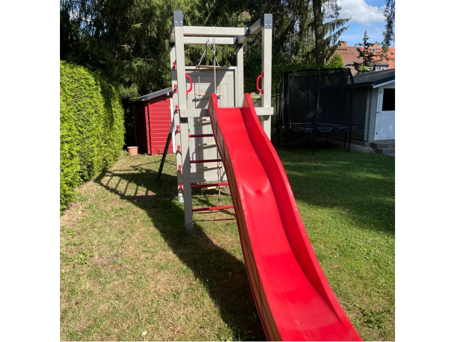 Ein graues Klettergerüst mit roter Rutsche im Garten