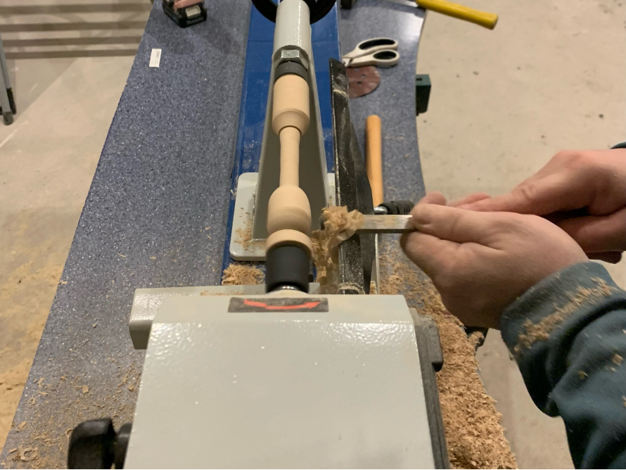 Person bearbeitet Holz an Drehbank mit Werkzeug