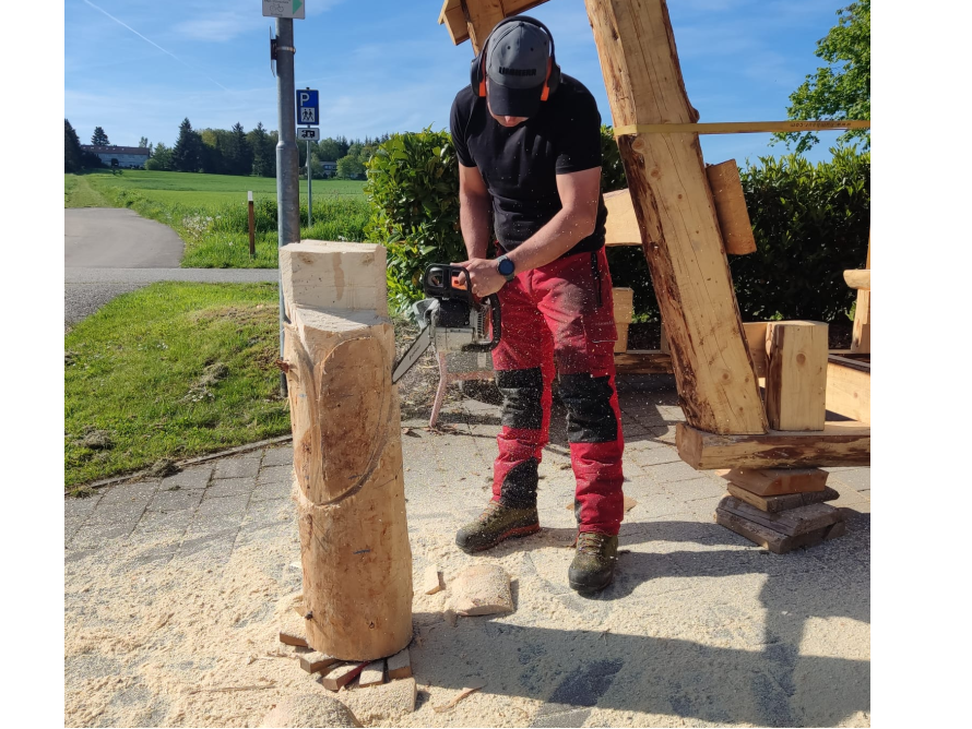 Person bearbeitet Holzstamm mit Kettensäge
