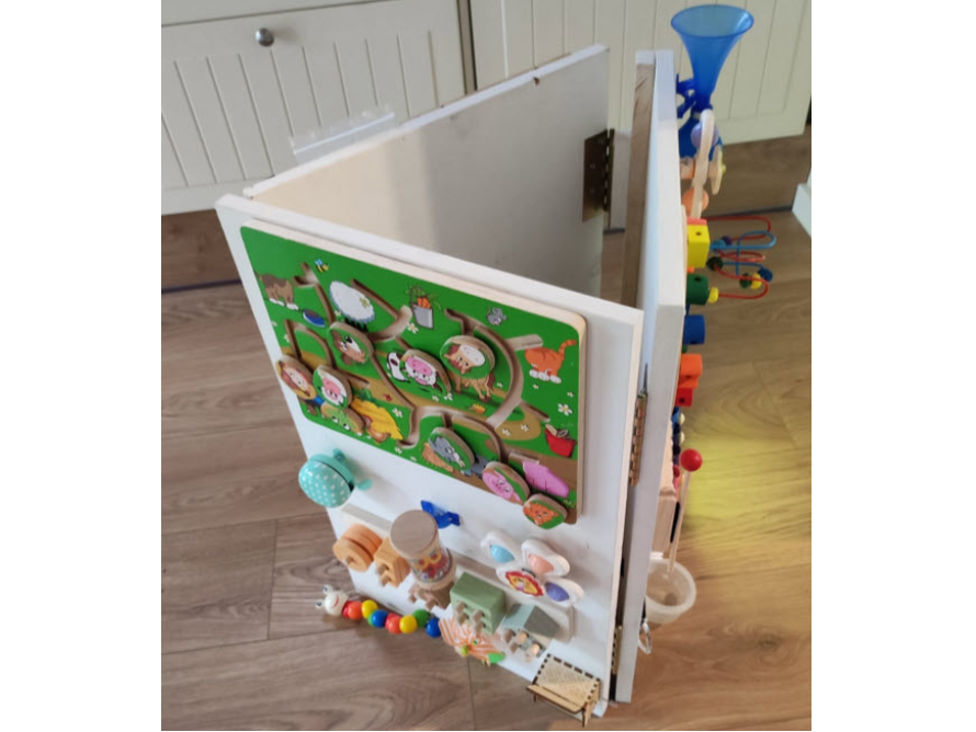 Ein weißes Spielhaus aus Holz mit verschiedenen motorischen Aktivitäten darauf.