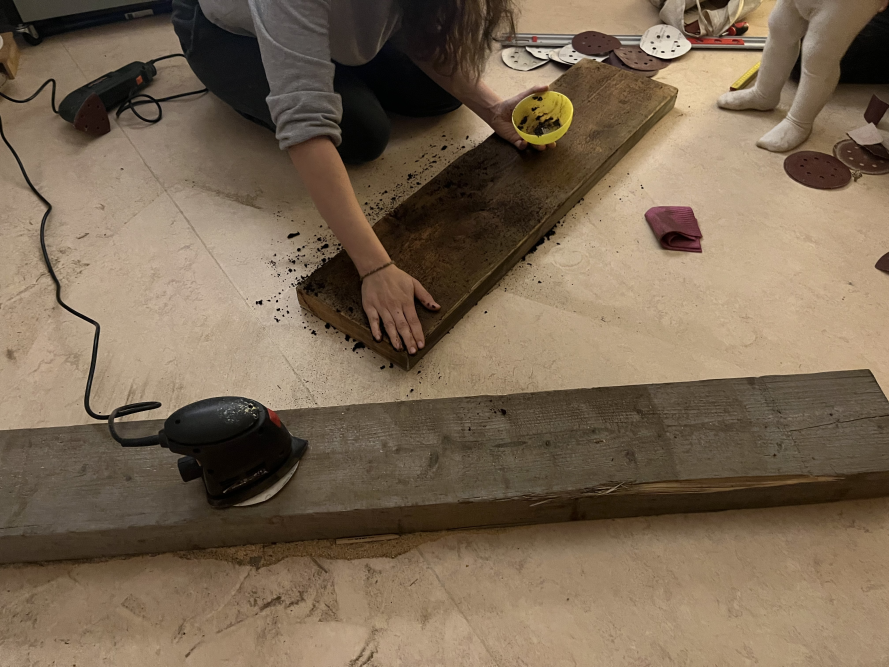 Person schleift Holzbrett mit Schleifmaschine