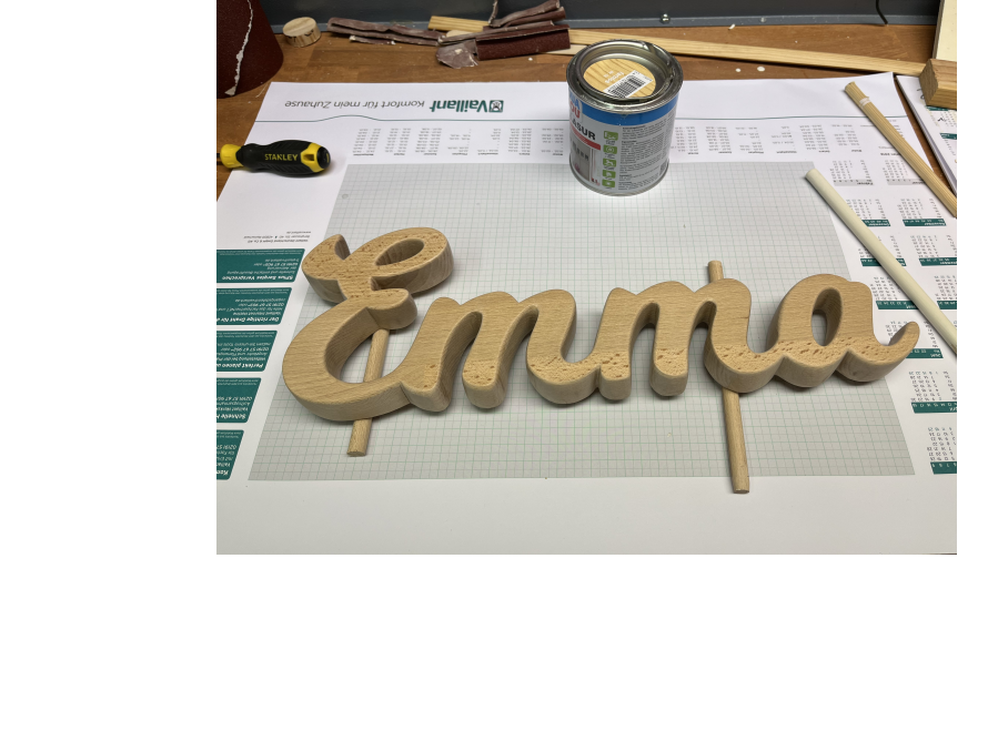 Der Schriftzug "Emma" aus Holz liegt auf einer Werkbank.