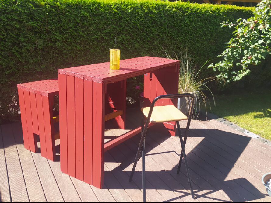 Ein roter selbstgebauter Gartentisch mit zwei Barhockern.