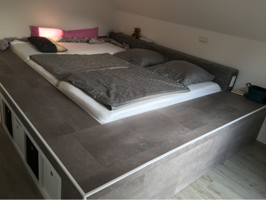 Ein Doppelbett mit grauer Bettwäsche auf einem Podest.