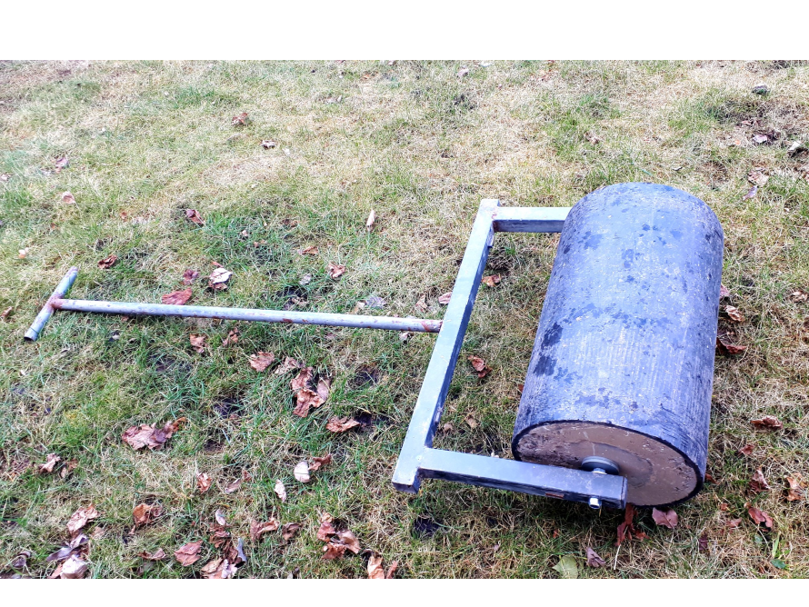 Eine Rasenwalze liegt auf einem Rasen.