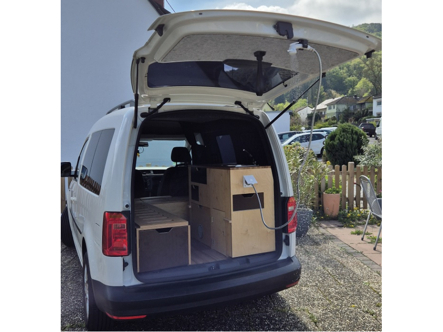 Ein weißer Van mit geöffnetem Kofferraum, der als Wohnmobil ausgebaut ist.