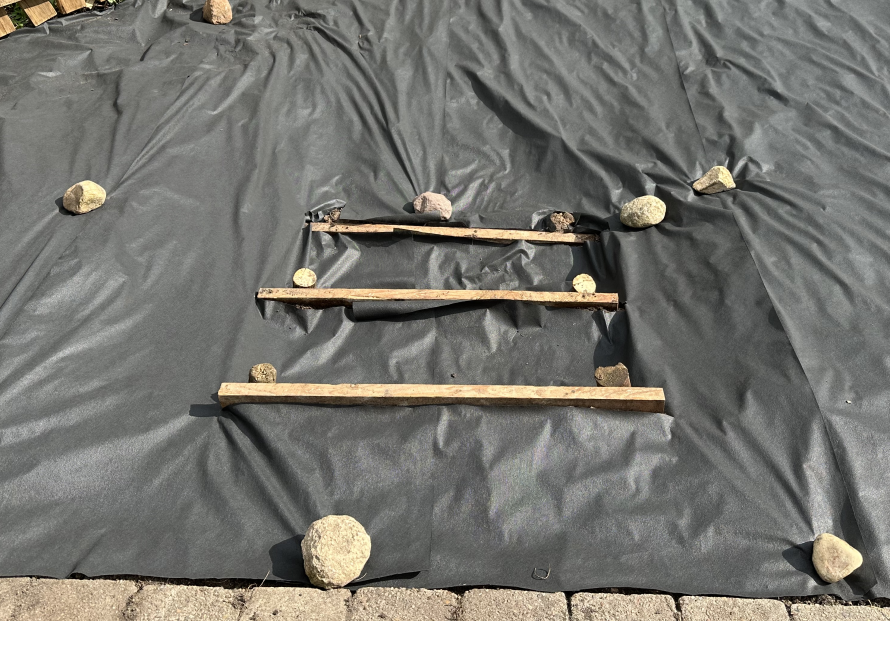 Schwarze Folie mit drei Holzlatten und Steinen