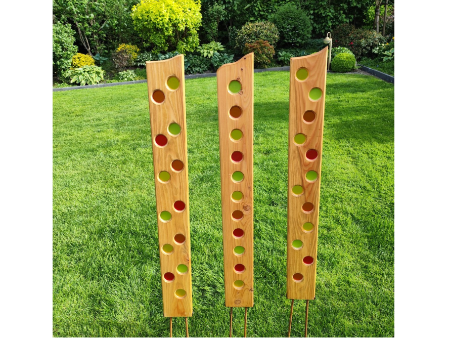 Drei hohe Holzlatten mit bunten Glaskreisen im Rasen