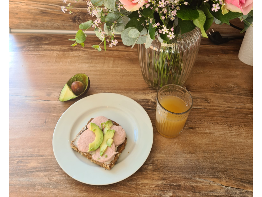 Ein belegtes Brot mit Avocado, ein Glas Saft und Blumen.