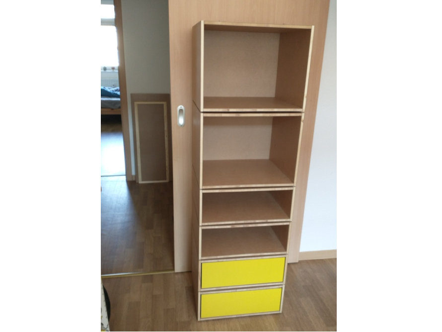 Schmales Regal aus Holz mit offenen Fächern und zwei gelben Schubladen.