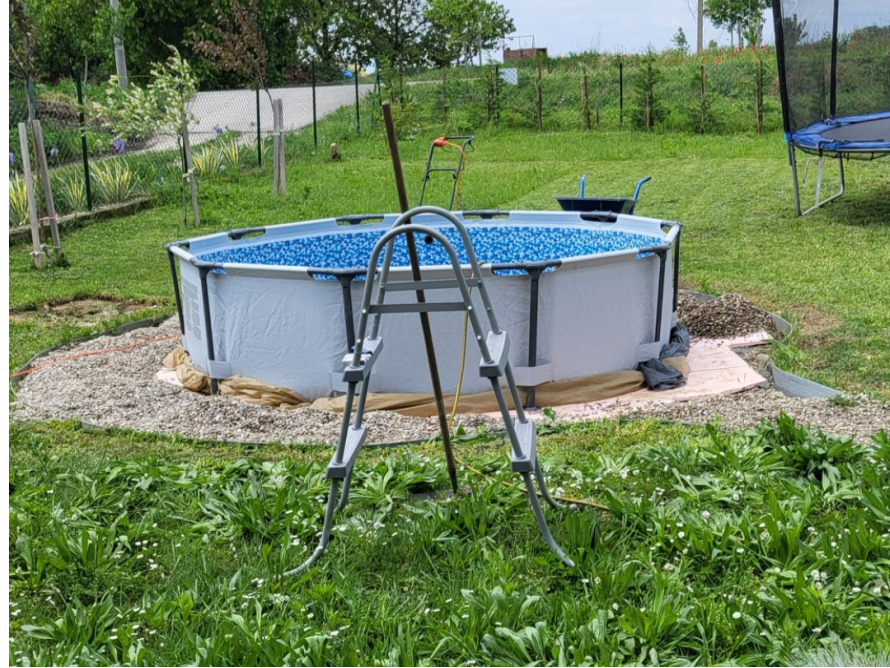 Ein Aufstellpool mit Leiter wird in einem Garten auf einer Kiesfläche aufgebaut.