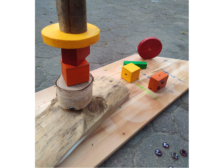 Bunte Holzbausteine und Holzstücke liegen auf einem Brett im Freien.