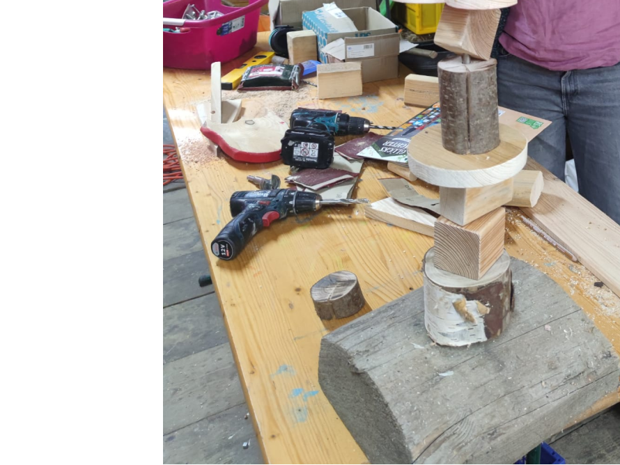 Eine unfertige Holzskulptur steht auf einer Werkbank neben zwei Akkuschraubern.