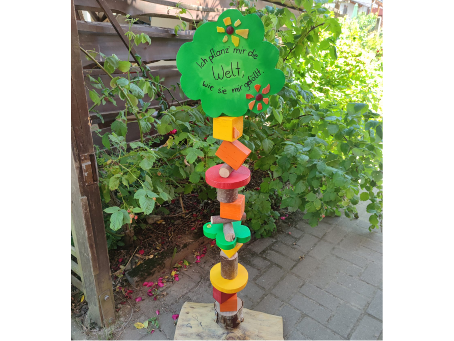 Bunte, selbstgemachte Holzskulptur mit Aufschrift steht im Garten.